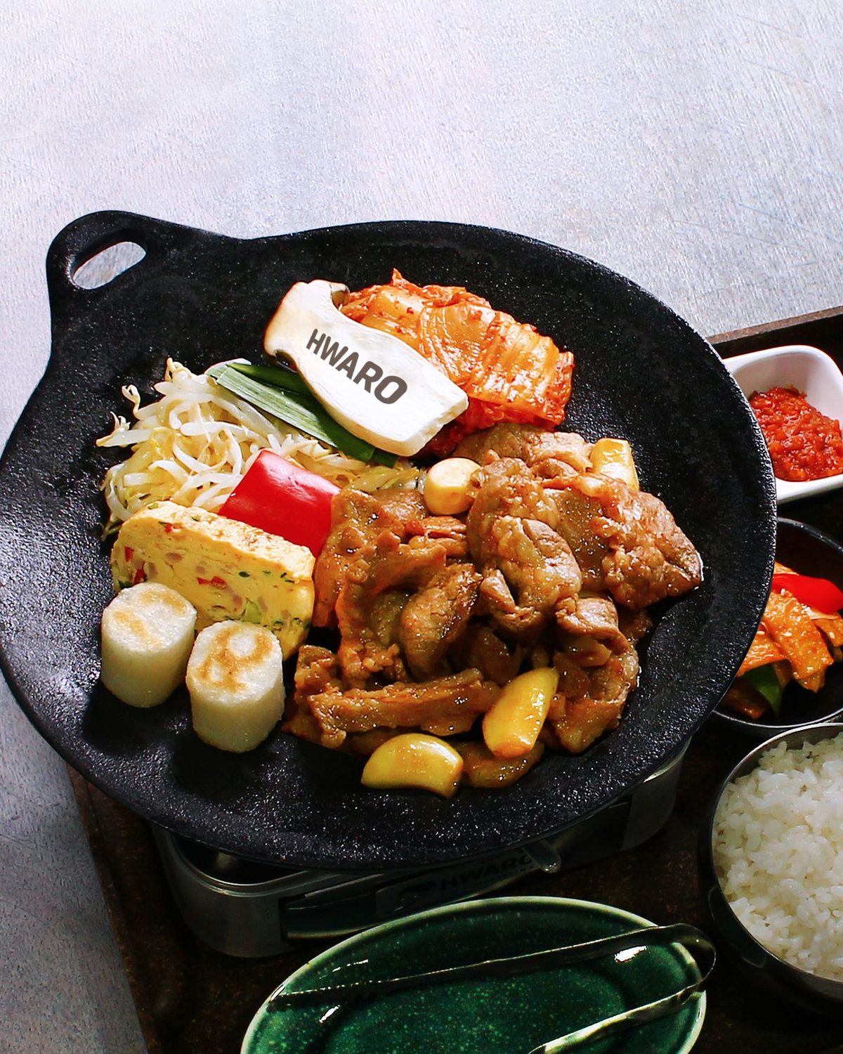 Dwaeji bulgogi searing on the Hwaro griddle with garlic, kimchi and rice cake